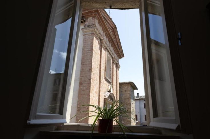 Scene viewed from a window inside a house, featuring a plant and a visible church outside.