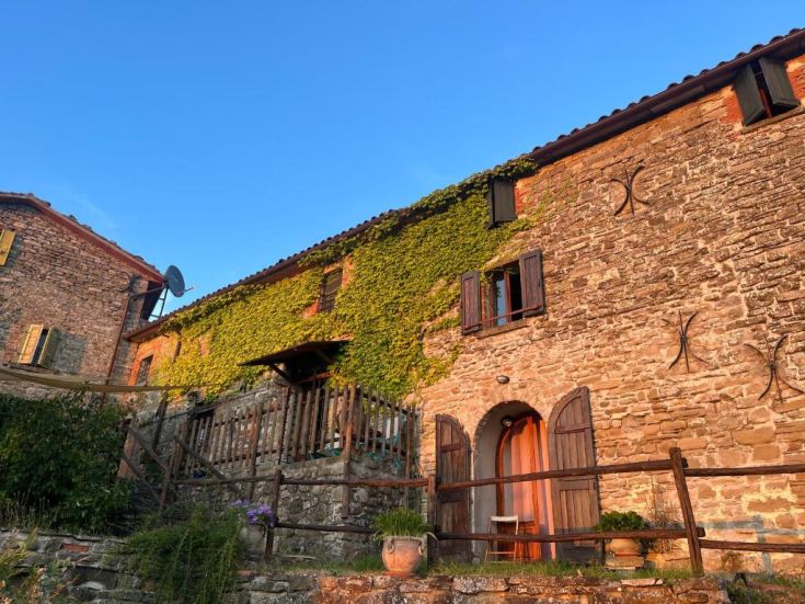 A farmhouse nestled in nature, surrounded by lush greenery under a clear sky.