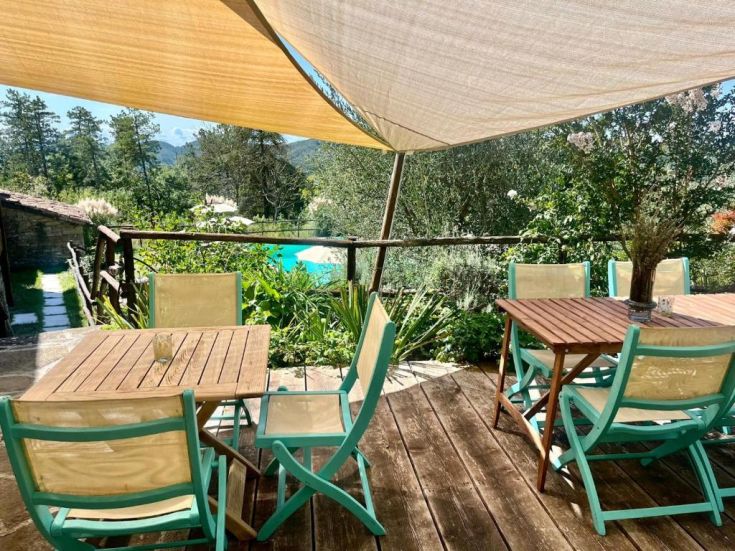 A well-furnished outdoor terrace with tables and chairs, surrounded by greenery and close to a swimming pool.