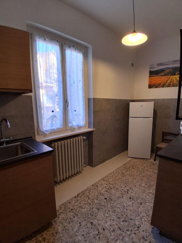 Spacious and bright kitchen with large windows, equipped with a refrigerator and practical wooden shelves.