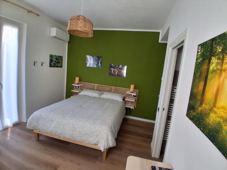 A simple and cozy double bedroom with green tones on the walls and wooden details.