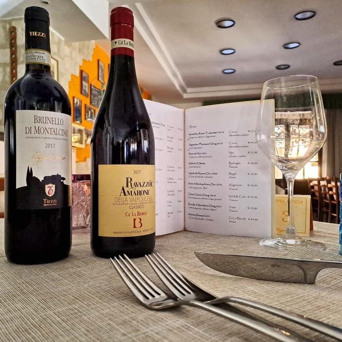 tavolo apparecchiato con vini rossi e menù aperto 