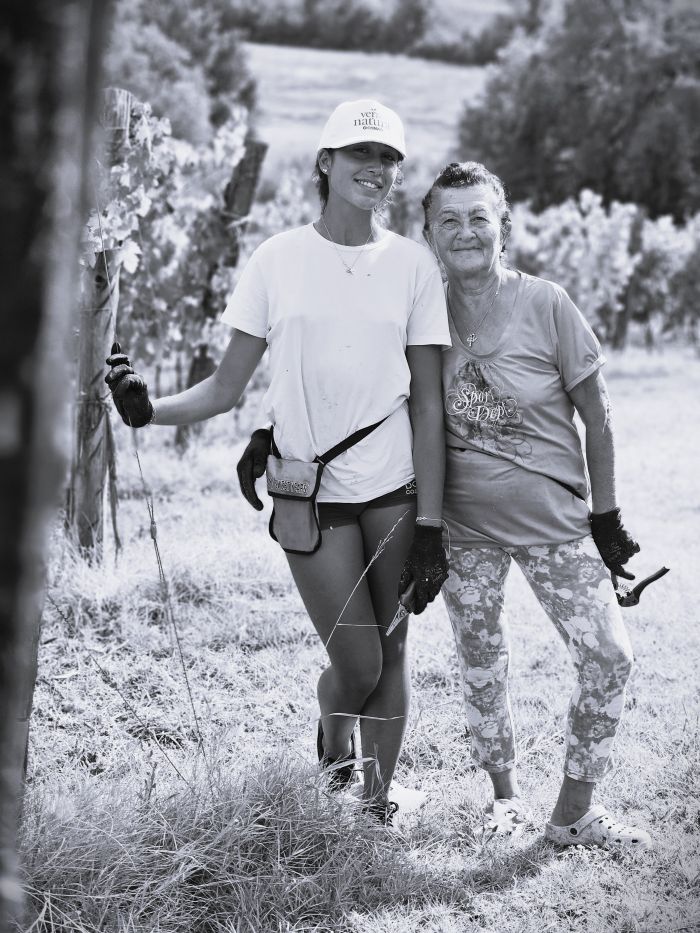 Nonna Maria e la nipote Jessica tra i filari, durante la vendemmia, raccolgono grappoli e sorrisi. È un momento unico, dove il tempo rallenta e l’aria profuma di mosto e risate. Si lavora con le mani, ma anche con il cuore — tra racconti, scherzi e gesti antichi che parlano d’amore per la terra.