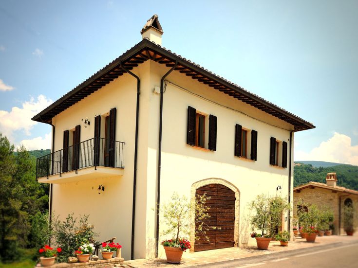 Una casa bianca con dettagli in legno, circondata da piante e fiori colorati.
