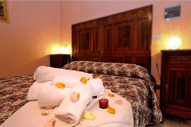 Camera accogliente con biancheria semplice e petali di rosa, ideale per un soggiorno tranquillo.