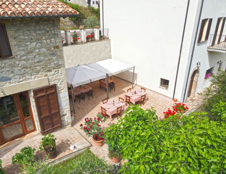 Area esterna dell'Agriturismo Casa Brunori, circondata da vegetazione, con tavoli e ombrelloni per il relax.