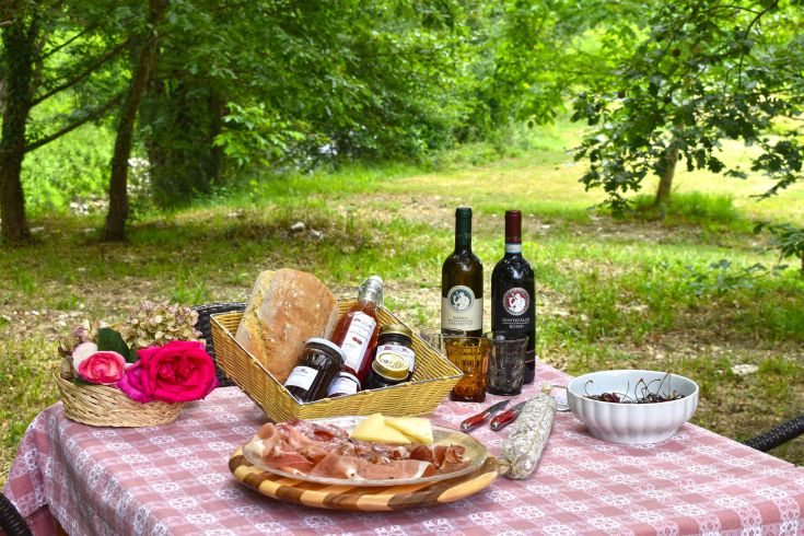 Un tavolo disposto all'aperto con piatti tipici, vini e fiori, all'interno di un contesto naturale.
