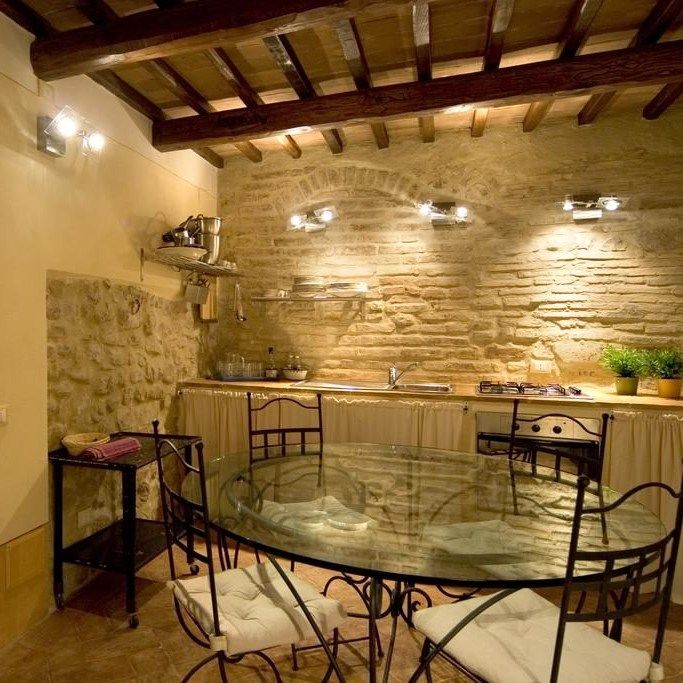 Rustic kitchen with stone walls, round glass table, and simple decor. Warm and cozy atmosphere.