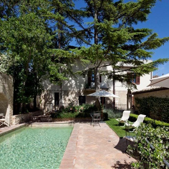 Landscape of a garden with a pool, surrounded by trees and an elegant mansion.