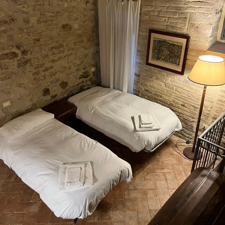 Cozy intimate room with two single beds, featuring stone walls and a floor lamp for lighting.