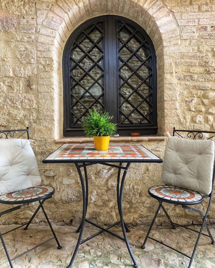 An outdoor relaxation area with a table and chairs, surrounded by stone walls and a window letting in natural light.