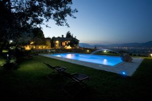 Una piscina illuminata al tramonto, circondata da alberi e piante, che crea un'atmosfera tranquilla.