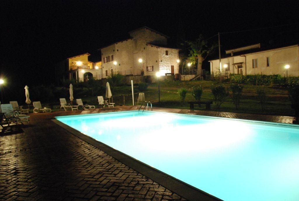 Una piscina illuminata in un casale storico, circondata da un giardino curato, ideale per le serate estive.