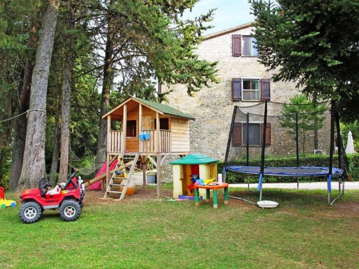 Un jardin avec des jeux pour enfants, une petite maison et un trampoline, entouré de verdure.