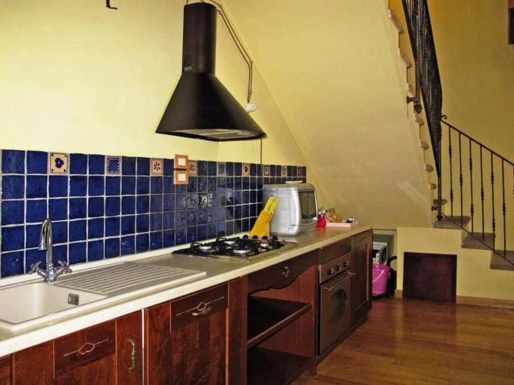 Cuisine moderne avec des carreaux bleus, des éléments en bois et un escalier menant à l'étage supérieur.