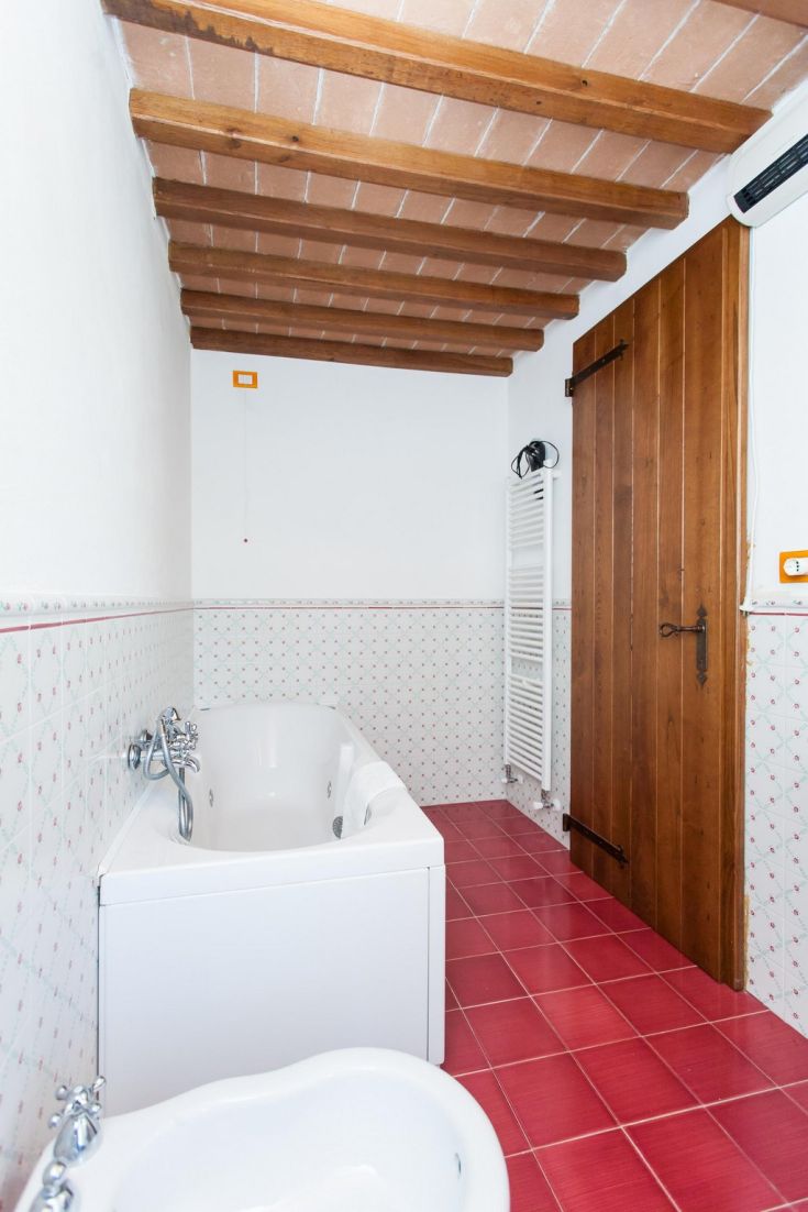Une salle de bain simple avec une baignoire blanche, des carreaux clairs et un plafond en bois.
