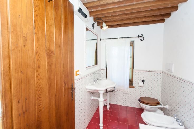 Une salle de bain simple avec un design en bois clair et carrelage, dotée d'une fenêtre et d'un lavabo classique.
