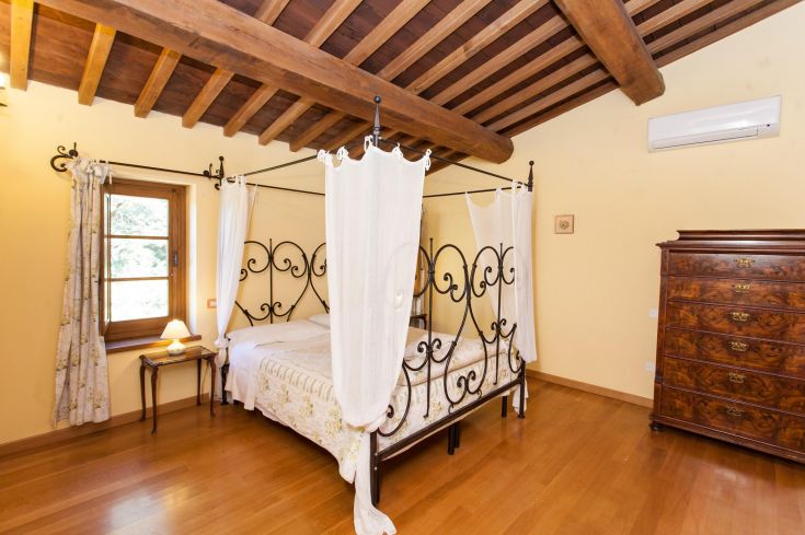 Chambre élégante avec un lit à baldaquin, des poutres apparentes et un décor classique, idéale pour des moments de tranquillité.