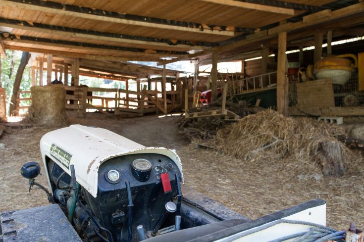 Un tracteur dans une grange, entouré d'outils agricoles et de bottes de paille.
