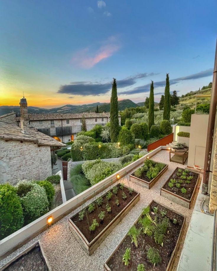 Sunset scene in Assisi, surrounded by gardens and vegetation near historic buildings.