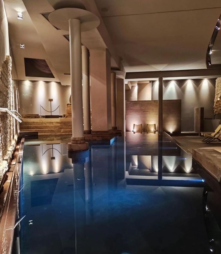 An indoor wellness area featuring a pool, softly lit by gentle lights, with contemporary-style columns.