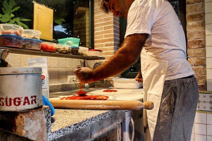 Un chef pétrit la pâte à pizza dans une cuisine simple et accueillante.