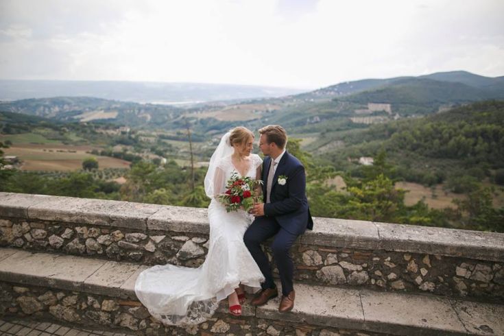 Un couple romantique de nouveaux mariés posant affectueusement devant un mur, entouré de collines vertes.