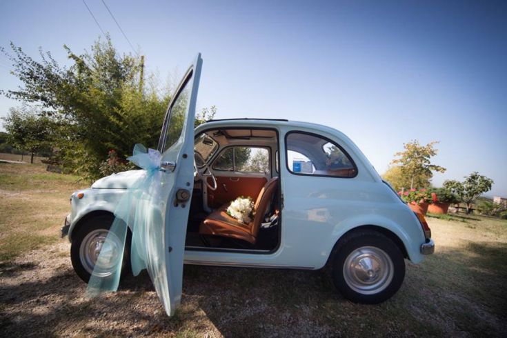 Une Fiat 500 décorée avec des rubans dans une scène de mariage entourée de verdure.