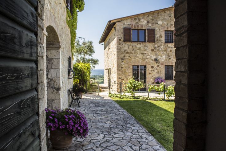 Un agriturismo pittoresque entouré de verdure, avec un jardin et des collines ondulantes.