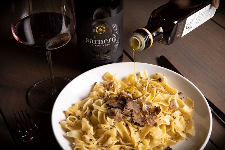 Une assiette de pâtes aux truffes, arrosée d'huile d'olive, servie avec un verre de vin rouge.