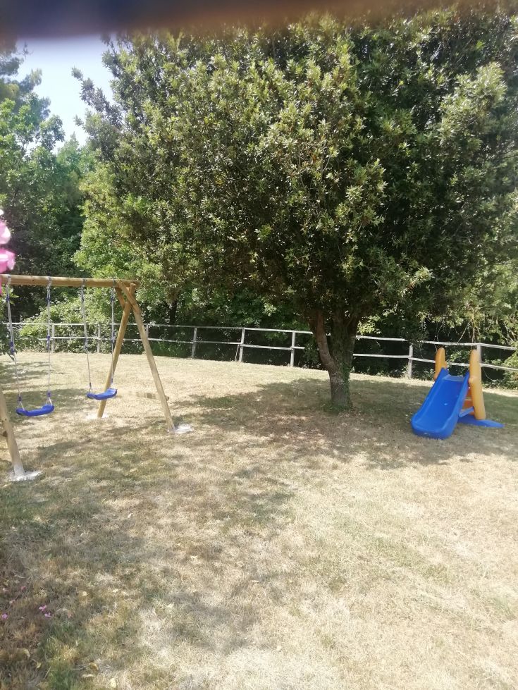 An outdoor playground with swings and a slide, surrounded by trees and a relaxed atmosphere.