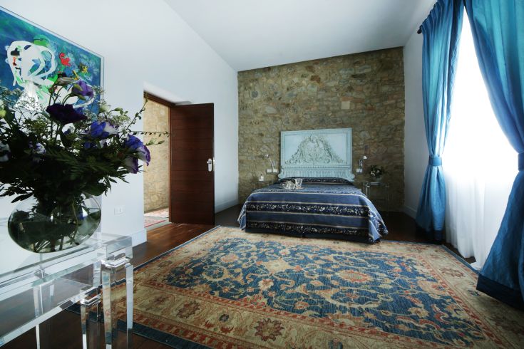 Camera semplice con dettagli in pietra e tende blu, situata nella tranquilla Tenuta Ponziani.