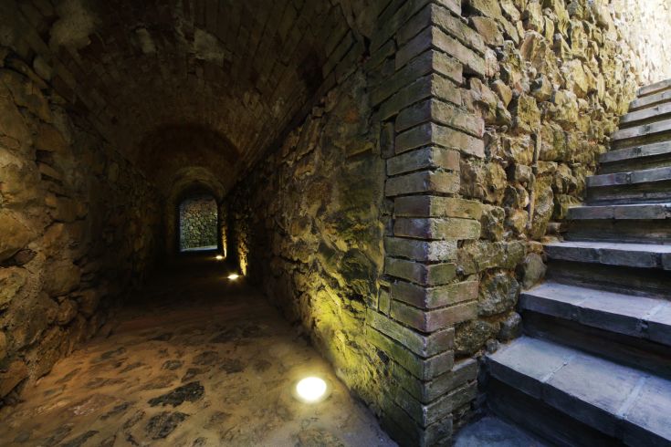 Corridoio con pareti in pietra e scale, illuminato da luci soft.