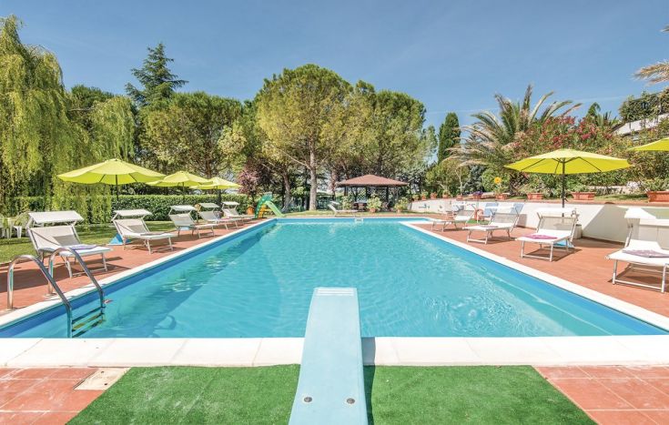 Una piscina tranquilla immersa nel verde, circondata da alberi e ombrelloni a disposizione.