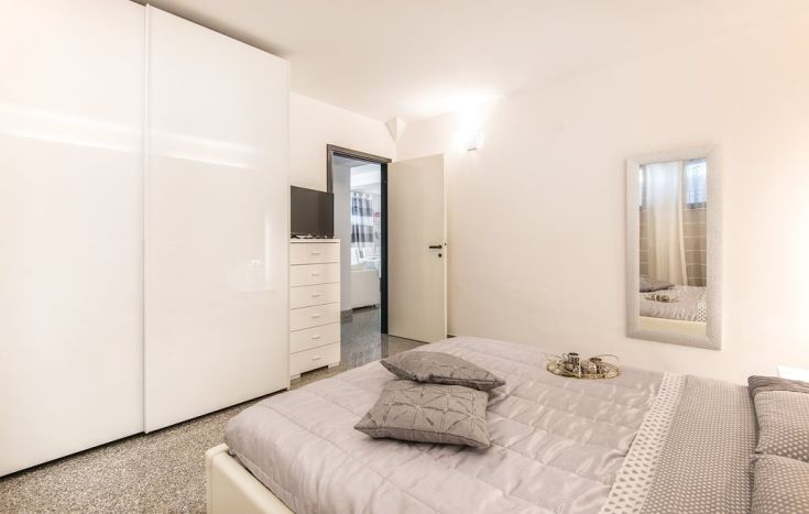 Camera da letto moderna e luminosa con armadio bianco, letto matrimoniale e specchio decorativo.