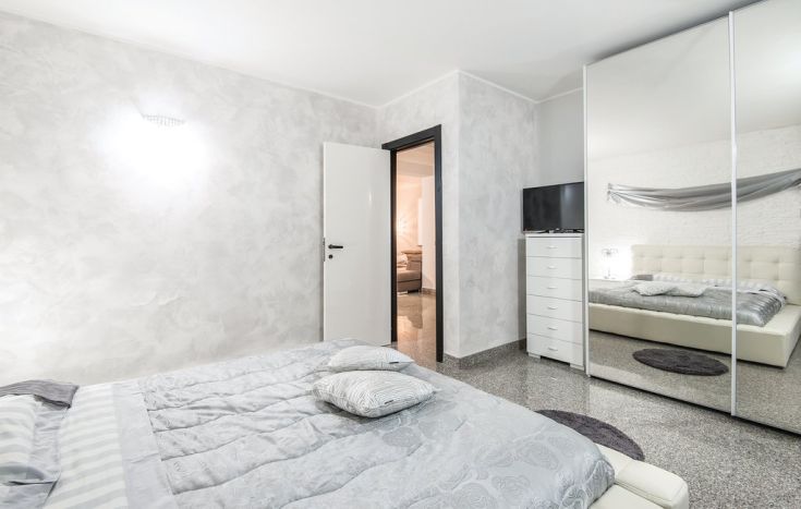 Interno sobrio di una camera da letto con pareti grigie e un grande specchio.