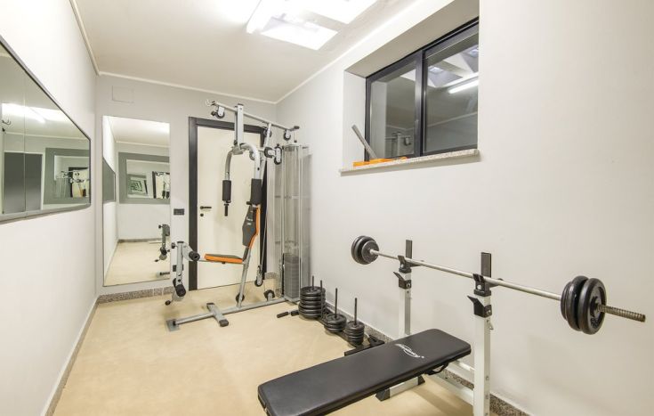 Una palestra di dimensioni contenute, attrezzata con apparecchi per l'allenamento e uno specchio, adatta per l'uso domestico.