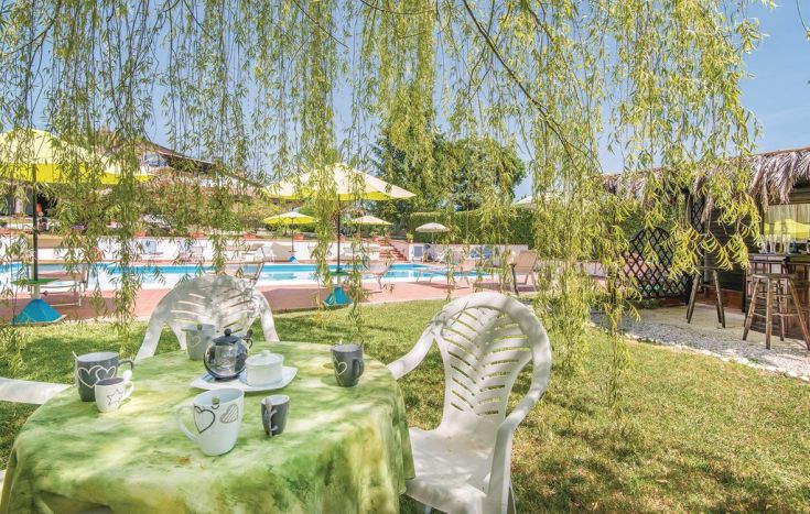 Un'area relax tranquilla con un tavolo e alcune tazze, immersa nel verde e con una piscina visibile in lontananza.