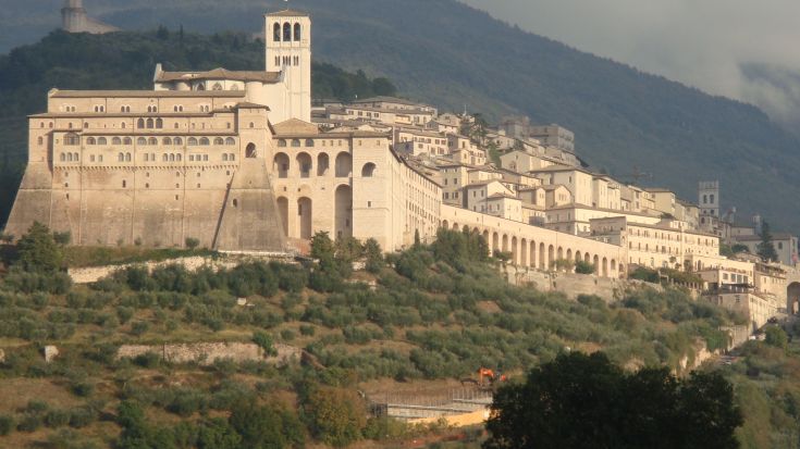 Un panorama della Basilica di San Francesco , circondata da verdi colline e un cielo leggermente nuvoloso. Un luogo carico di storia e spiritualità.