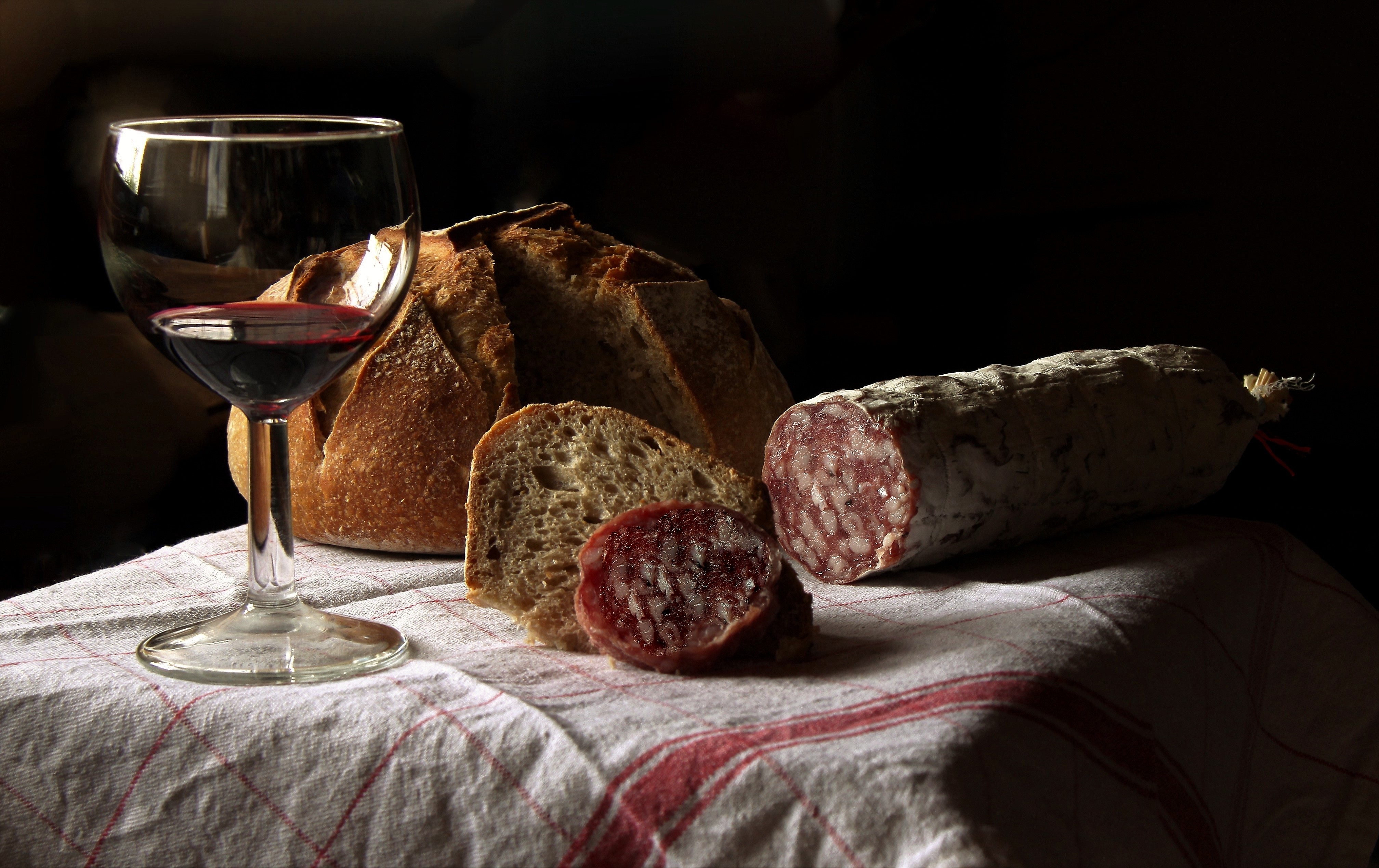 Una tavola rustica con pane, salame e un calice di vino rosso in un ambiente accogliente.