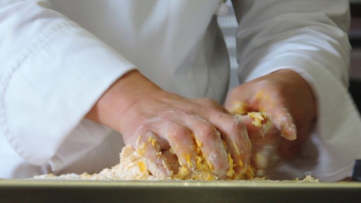 Le mani di un cuoco mentre impasta ingredienti in cucina, un momento fondamentale nella preparazione.