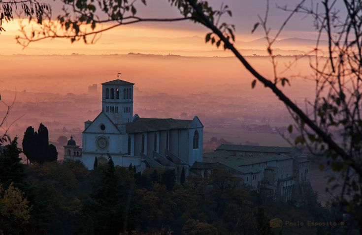 Una scena della Basilica di San Francesco ad Assisi al tramonto, con una leggera nebbia che avvolge l'edificio.