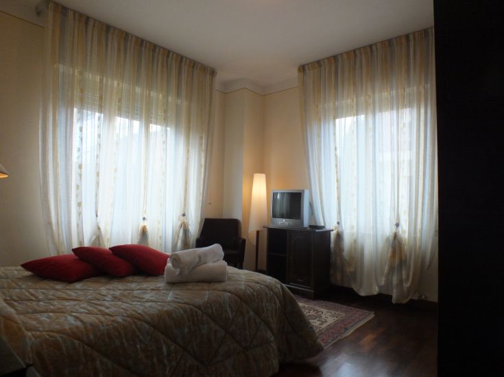 Stanza accogliente con letto matrimoniale, TV e tende chiare, ideale per un soggiorno tranquillo.