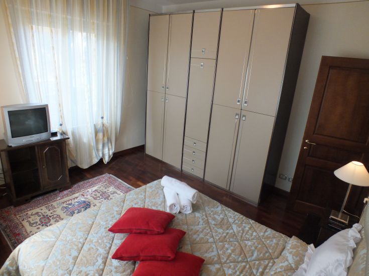 Camera da letto moderna e confortevole, dotata di armadio, TV e letti con cuscini rossi.