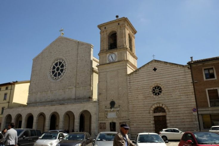 Scena della chiesa con campanile e architettura storica, circondata da automobili.