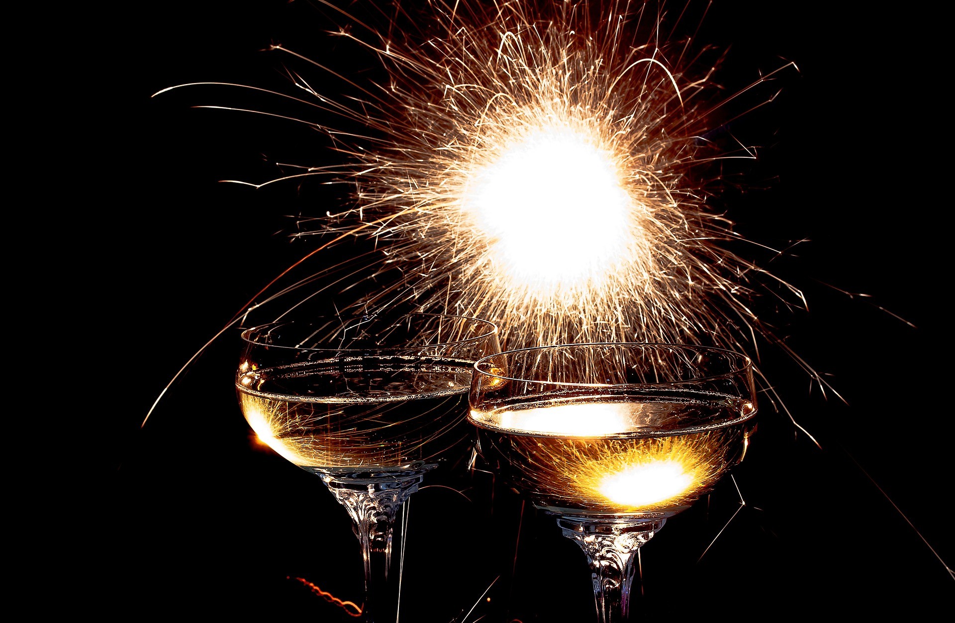 Due coppe di champagne brillano mentre un fuoco d'artificio esplode sullo sfondo.