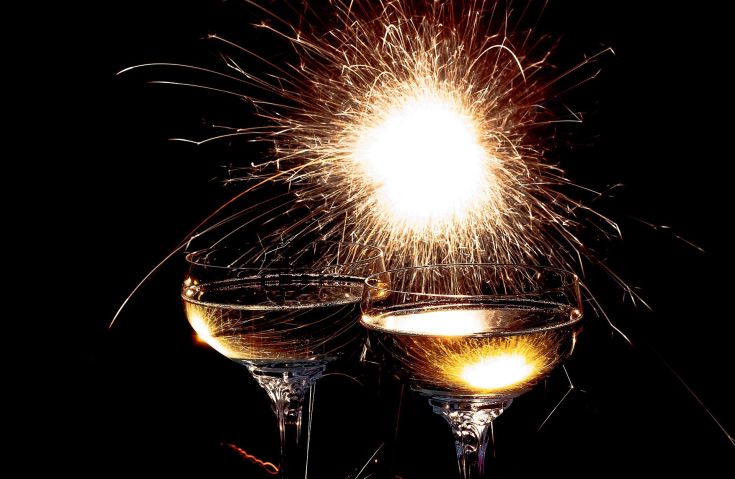 Due coppe di champagne brillano mentre un fuoco d'artificio esplode sullo sfondo.