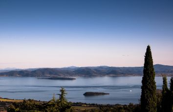 Un panorama tranquillo di un lago circondato da dolci colline e alberi, sotto un cielo che sfuma in toni di blu.