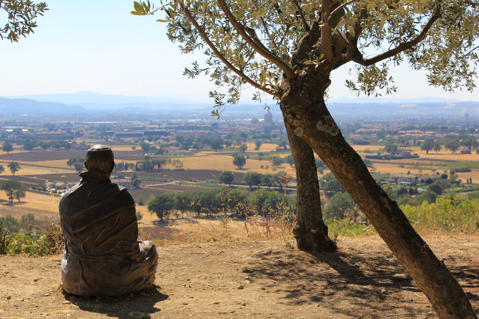 Una scultura in ferro di un uomo in meditazione, sotto un albero d'ulivo che osserva la valle Umbra.