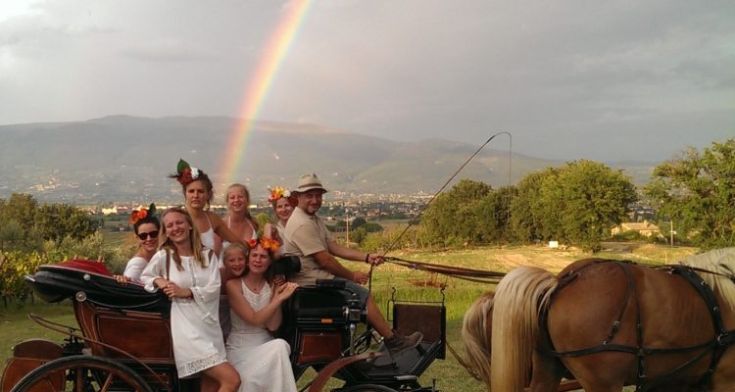 Un gruppo di persone sorridenti si trova su una carrozza, mentre un arcobaleno si staglia nel cielo.